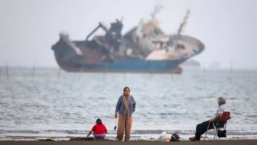 People gather on a beach, as a vessel in the Strait of Hormuz is visible, near the beach of Bandar Abbas, Iran. 31 May, 2026. 
